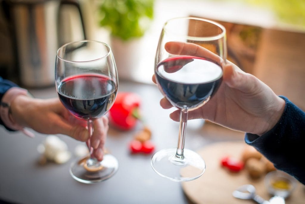 Close up photo of two people toasting with red wine